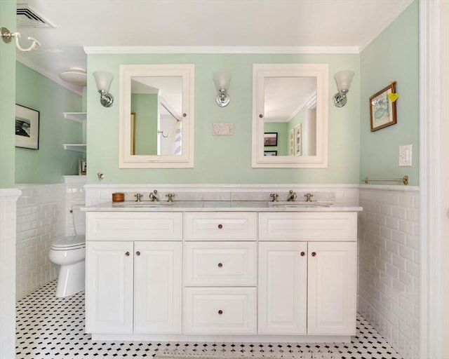 bathroom featuring a sink, ornamental molding, toilet, and tile walls