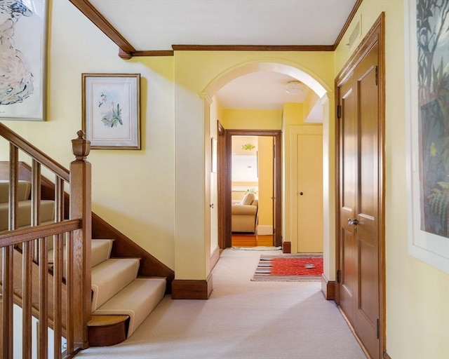 corridor with light colored carpet, arched walkways, crown molding, and stairway