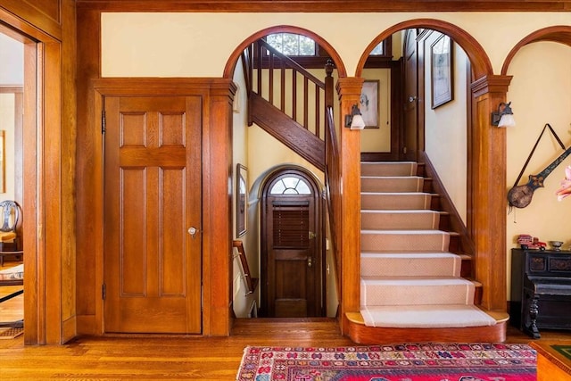 entryway with arched walkways, wood finished floors, and stairway