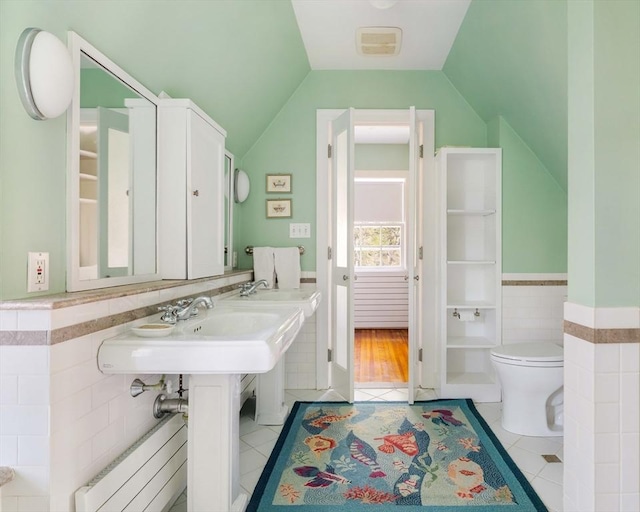 bathroom with tile patterned flooring, toilet, radiator heating unit, tile walls, and vaulted ceiling