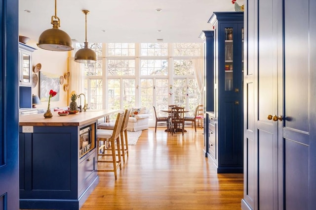 kitchen featuring stainless steel microwave, light wood-style flooring, blue cabinets, and butcher block counters