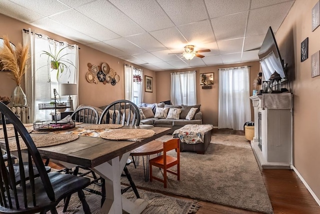 dining area with dark wood-type flooring, a drop ceiling, and ceiling fan