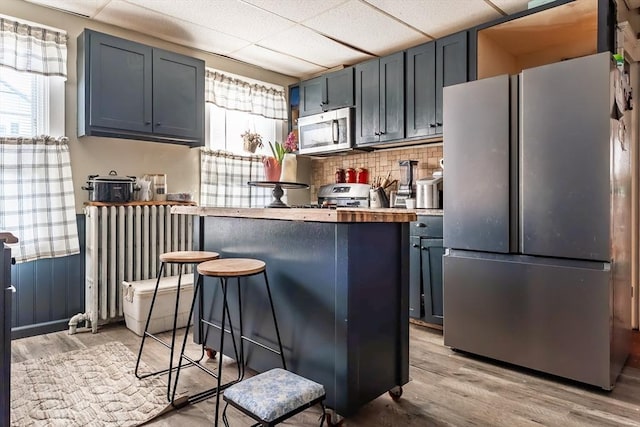 kitchen featuring light hardwood / wood-style flooring, a breakfast bar, appliances with stainless steel finishes, a drop ceiling, and kitchen peninsula