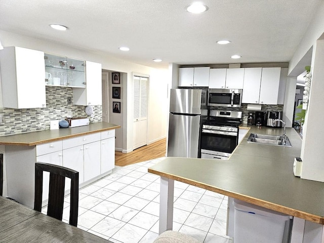 kitchen featuring a peninsula, a sink, decorative backsplash, stainless steel appliances, and white cabinets