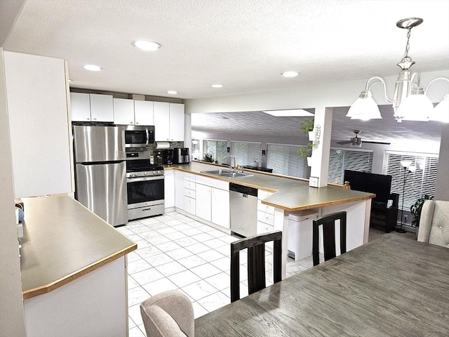 kitchen with ceiling fan with notable chandelier, stainless steel appliances, hanging light fixtures, white cabinetry, and a sink