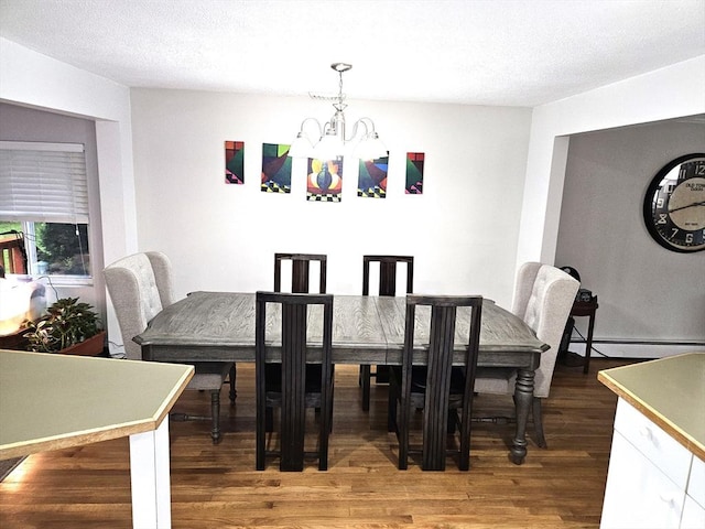 dining area with a notable chandelier, a baseboard radiator, a textured ceiling, and wood finished floors