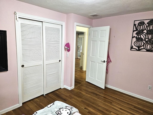 unfurnished bedroom featuring dark wood finished floors, a textured ceiling, baseboards, and a closet