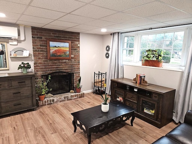 living area with baseboards, a fireplace, a drop ceiling, an AC wall unit, and light wood-style floors