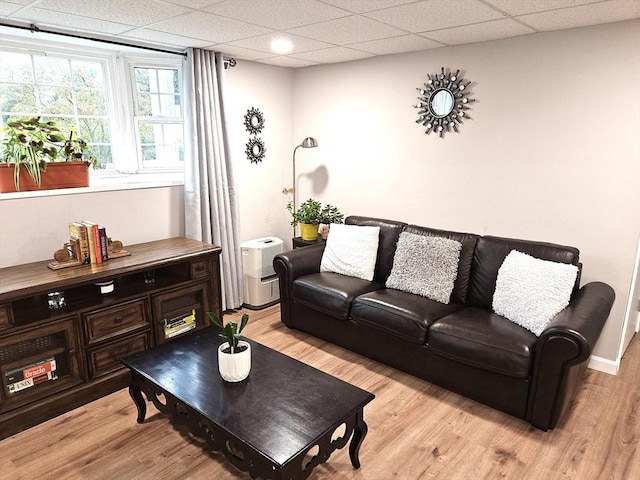 living area with light wood finished floors, a drop ceiling, and baseboards