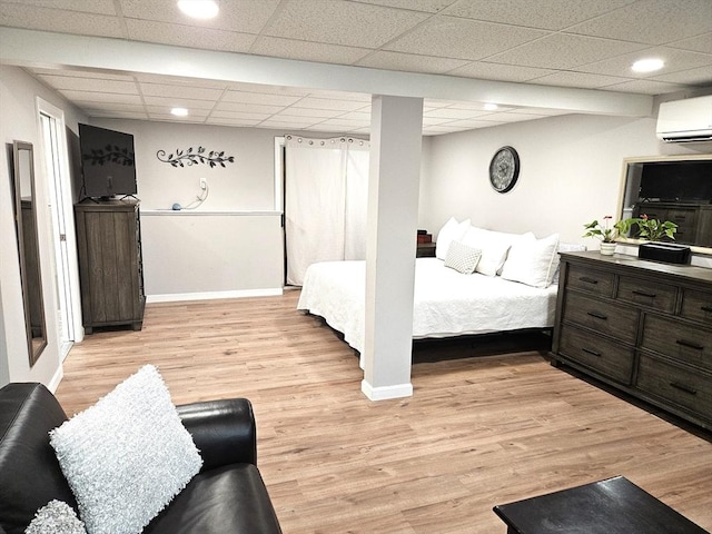 bedroom featuring a wall unit AC, baseboards, light wood-type flooring, and a drop ceiling