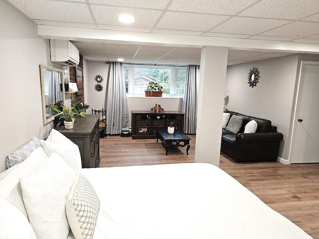 bedroom featuring baseboards, a paneled ceiling, light wood-style flooring, and a wall mounted AC