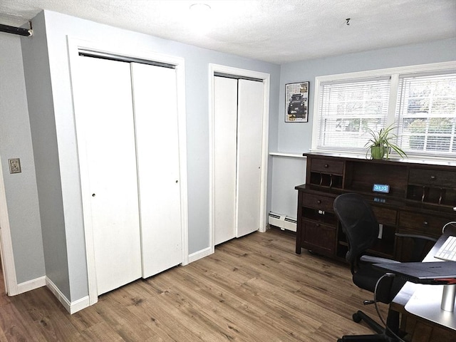 office space with a baseboard heating unit, baseboards, a textured ceiling, and wood finished floors