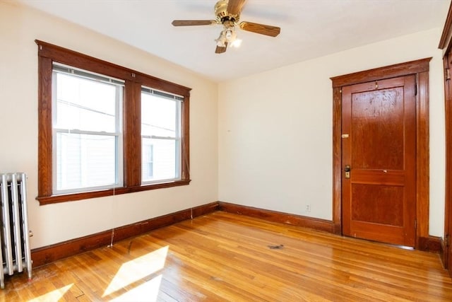 spare room with ceiling fan, radiator, baseboards, and light wood-style floors