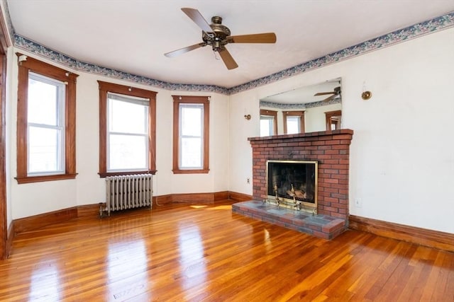 unfurnished living room featuring baseboards, a brick fireplace, radiator heating unit, and hardwood / wood-style flooring