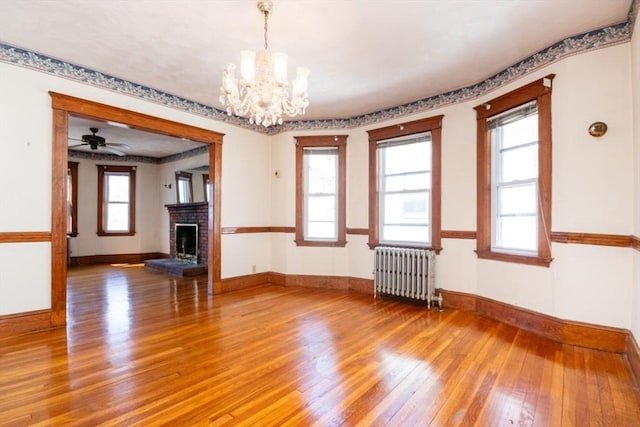 empty room with radiator, baseboards, light wood-style floors, and a brick fireplace