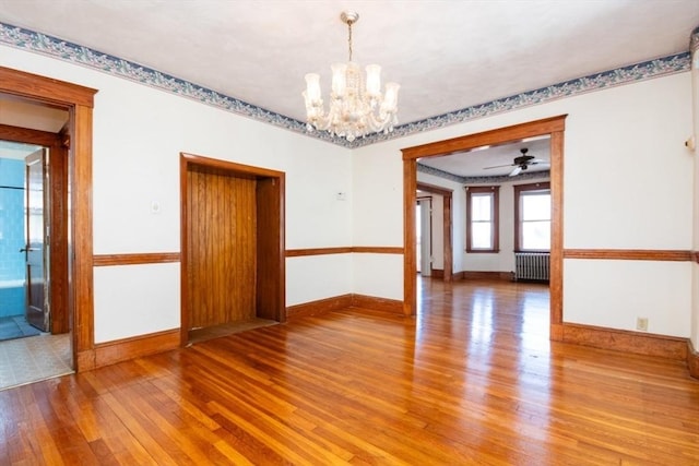 empty room featuring a notable chandelier, baseboards, radiator, and hardwood / wood-style flooring