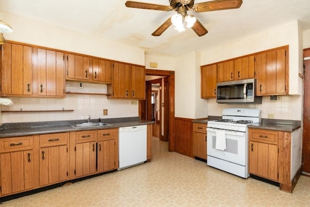 kitchen featuring a sink, dark countertops, white appliances, brown cabinetry, and light floors