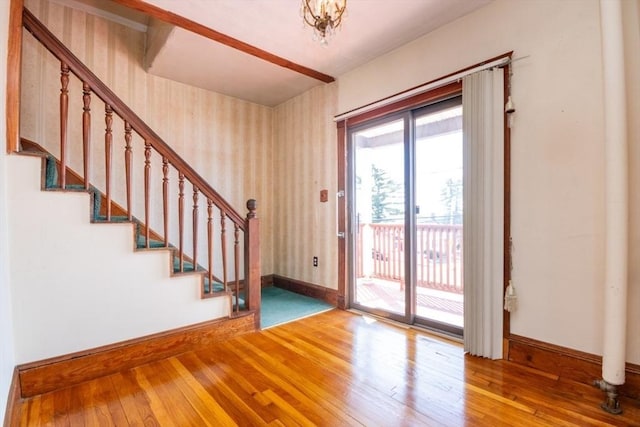 foyer entrance with stairway, baseboards, wallpapered walls, wood-type flooring, and a notable chandelier