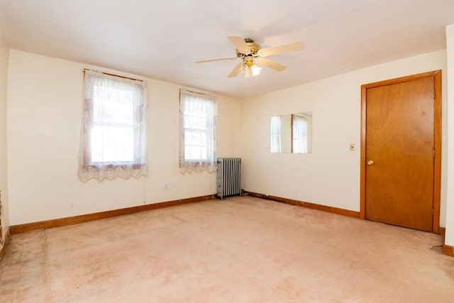 empty room featuring a ceiling fan, radiator heating unit, light colored carpet, and baseboards