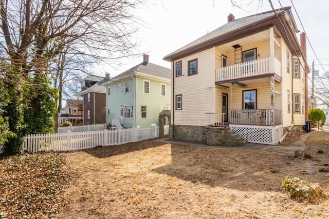 back of house featuring covered porch, a chimney, a balcony, and fence