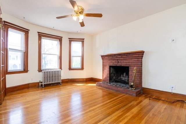 unfurnished living room featuring a brick fireplace, radiator, baseboards, and hardwood / wood-style flooring