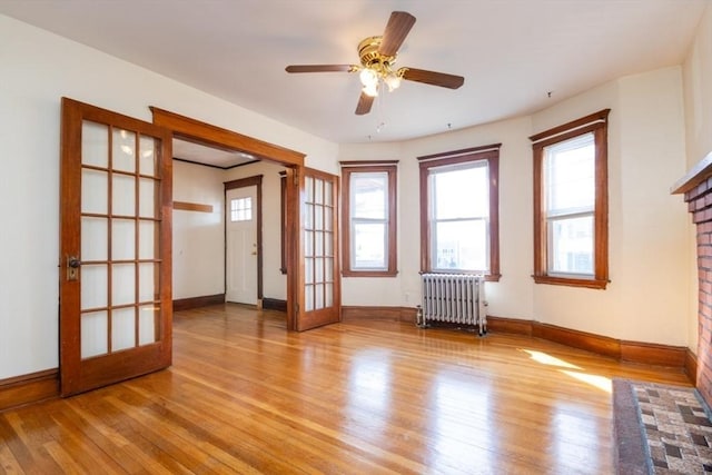 empty room featuring french doors, plenty of natural light, wood finished floors, and radiator heating unit