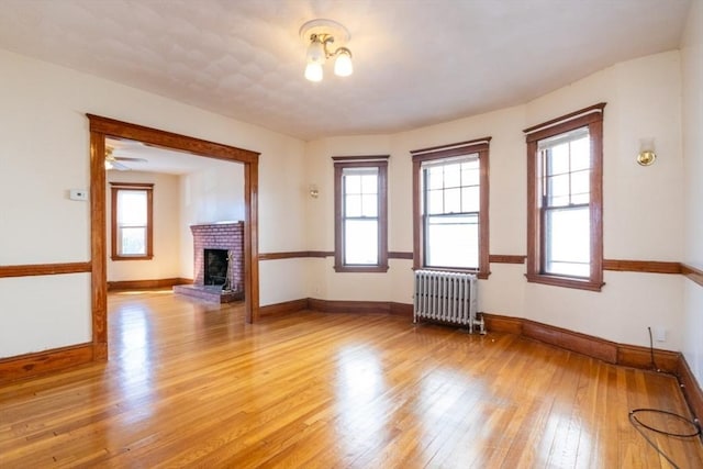 unfurnished living room featuring a fireplace, radiator, a healthy amount of sunlight, and light wood finished floors