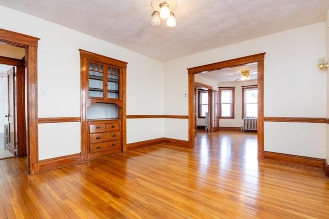 empty room with baseboards, radiator, and light wood finished floors