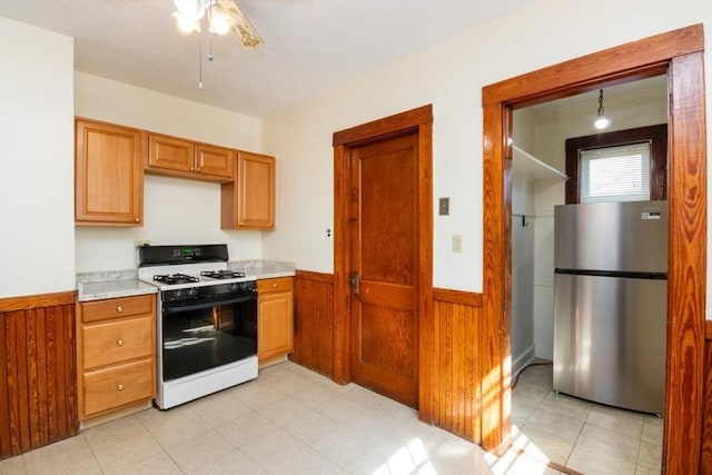 kitchen with gas range, wood walls, light countertops, wainscoting, and freestanding refrigerator