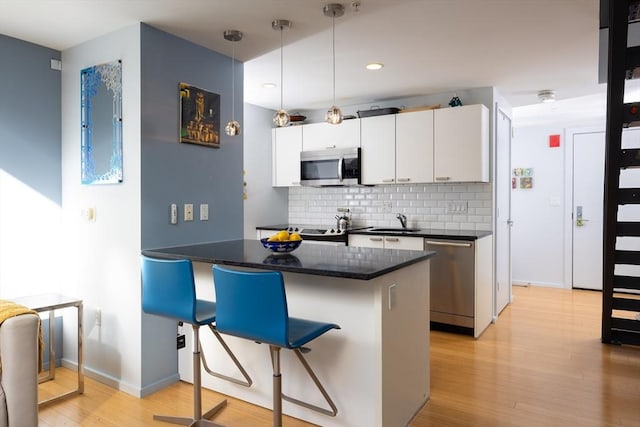 kitchen featuring a breakfast bar, white cabinetry, appliances with stainless steel finishes, pendant lighting, and backsplash