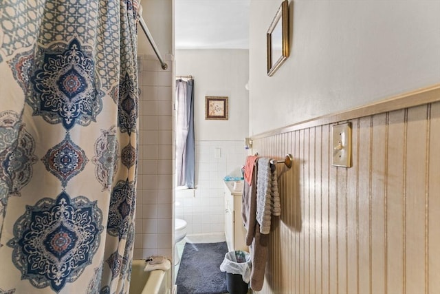 bathroom featuring a wainscoted wall, tile walls, toilet, and shower / bath combo with shower curtain