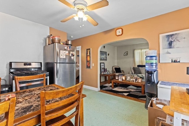 kitchen featuring arched walkways, appliances with stainless steel finishes, a ceiling fan, and baseboards