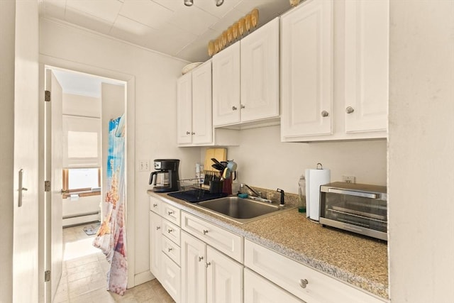 kitchen featuring a baseboard radiator, a toaster, a sink, white cabinets, and light countertops