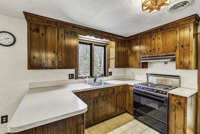 kitchen featuring under cabinet range hood, electric range, wallpapered walls, and a sink