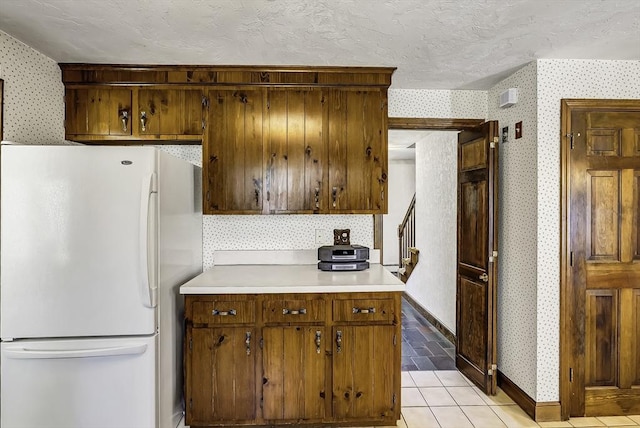 kitchen featuring freestanding refrigerator, baseboards, wallpapered walls, light countertops, and a textured ceiling