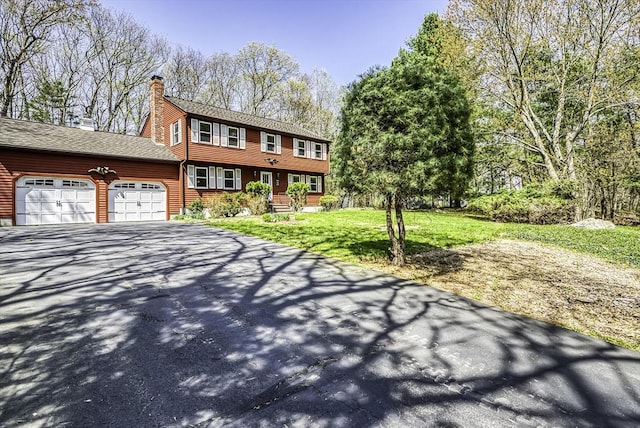 colonial home with an attached garage, driveway, a chimney, and a front lawn