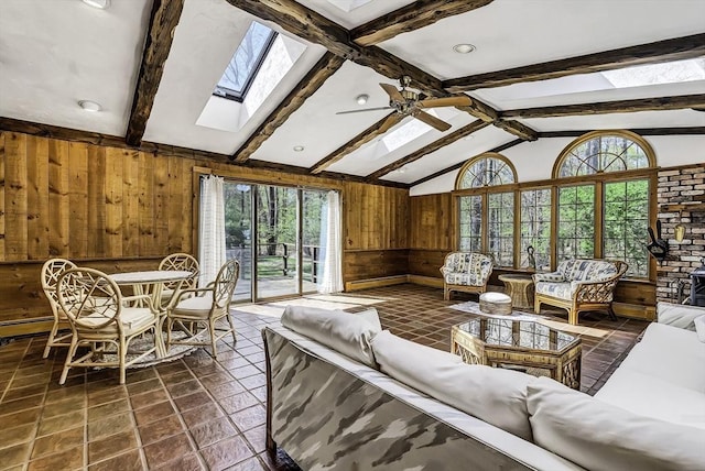 living area with wooden walls, a ceiling fan, a wealth of natural light, and lofted ceiling with skylight
