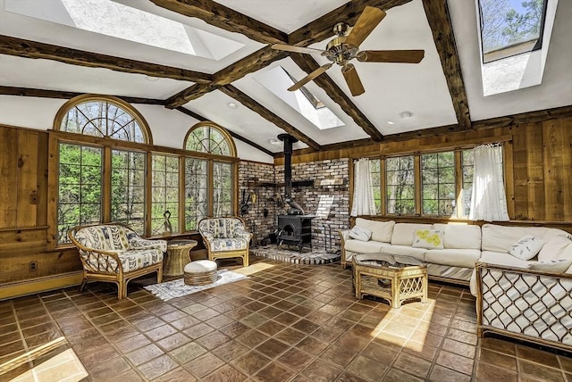 living room featuring a healthy amount of sunlight, ceiling fan, a wood stove, and lofted ceiling with skylight