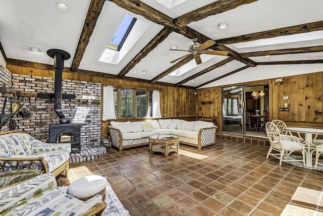 living area featuring vaulted ceiling with skylight, ceiling fan, a wood stove, wooden walls, and recessed lighting