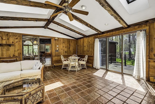 living area featuring wood walls, ceiling fan, and vaulted ceiling with skylight
