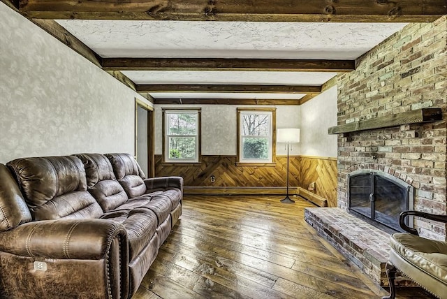 living room featuring beam ceiling, a fireplace, wood-type flooring, wood walls, and a wainscoted wall