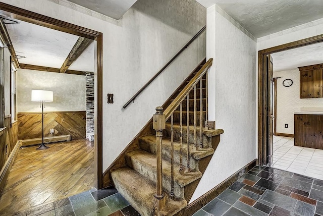 stairs with wooden walls, baseboards, ornamental molding, and stone finish flooring