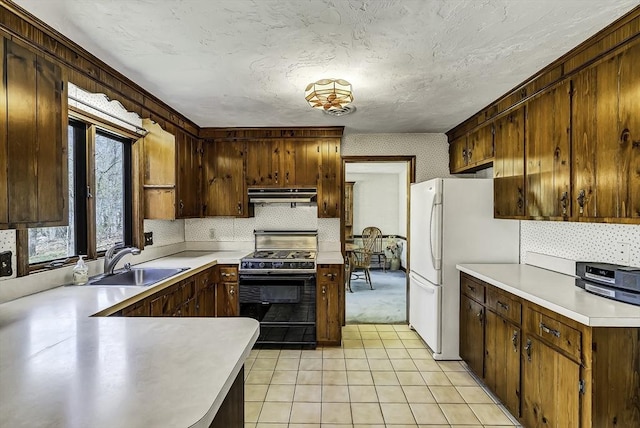 kitchen featuring freestanding refrigerator, light countertops, under cabinet range hood, a sink, and black range with gas cooktop