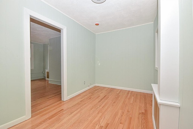 empty room with wood walls, light hardwood / wood-style floors, and ornamental molding