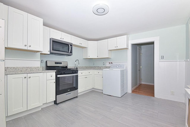 kitchen with light wood-type flooring, stainless steel appliances, white cabinetry, and washer / clothes dryer