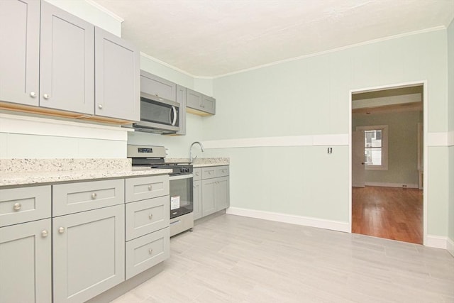 kitchen featuring stainless steel appliances, gray cabinets, crown molding, and light hardwood / wood-style flooring