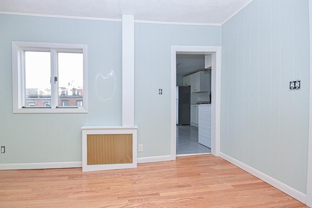 spare room featuring wood walls, light hardwood / wood-style flooring, and ornamental molding