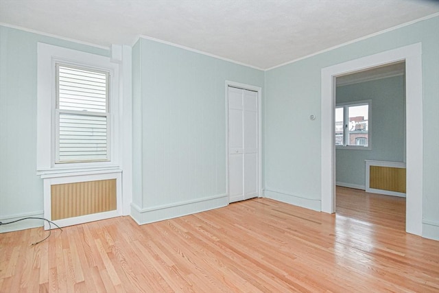 empty room with light wood-type flooring, radiator, and ornamental molding