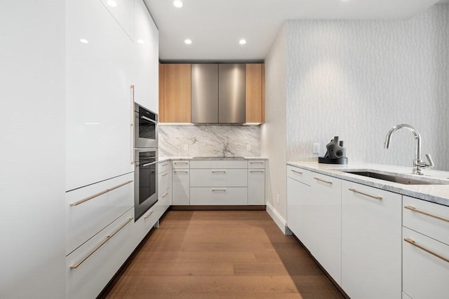 240 Devonshire St Unit 4210, Boston, MA 02110 - kitchen featuring a sink, light stone countertops, wood finished floors, decorative backsplash, and white cabinetry