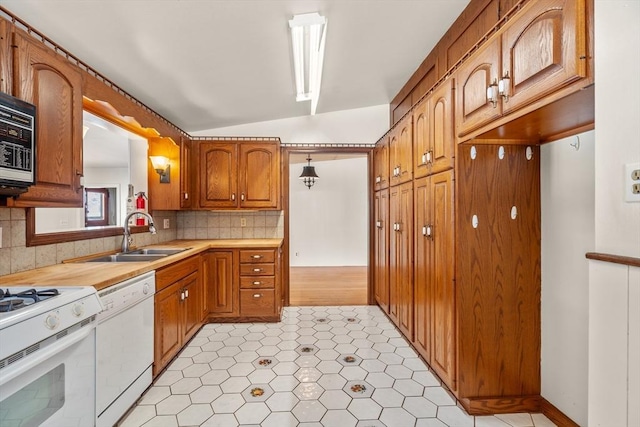 kitchen with white appliances, brown cabinetry, lofted ceiling, a sink, and backsplash